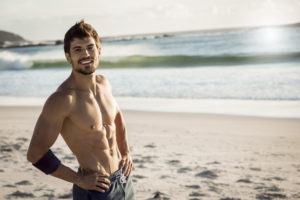strong fit man smiling and taking a break after hard workout,beautiful weather,sunny day,in the background waves splashing on the beach